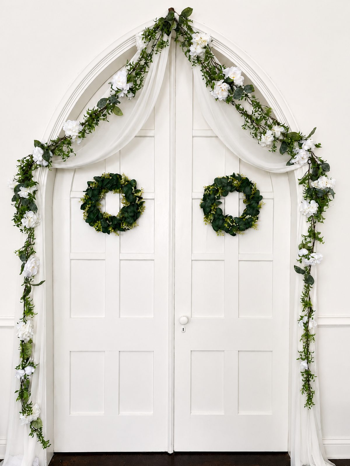 The chapel's arched doors decorated with white floral garlands for a wedding