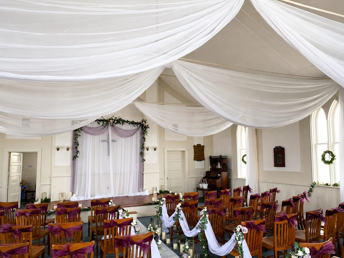 Chapel interior set for a wedding with draped ceiling, wooden chairs, and floral aisle